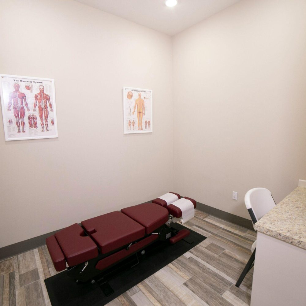 Ein ausgestatteter Behandlungsraum in der Chiropraxis Ulm mit einer professionellen Behandlungsliege, anatomischen Postern und einem Wirbelsäulenmodell zur Patientenaufklärung.