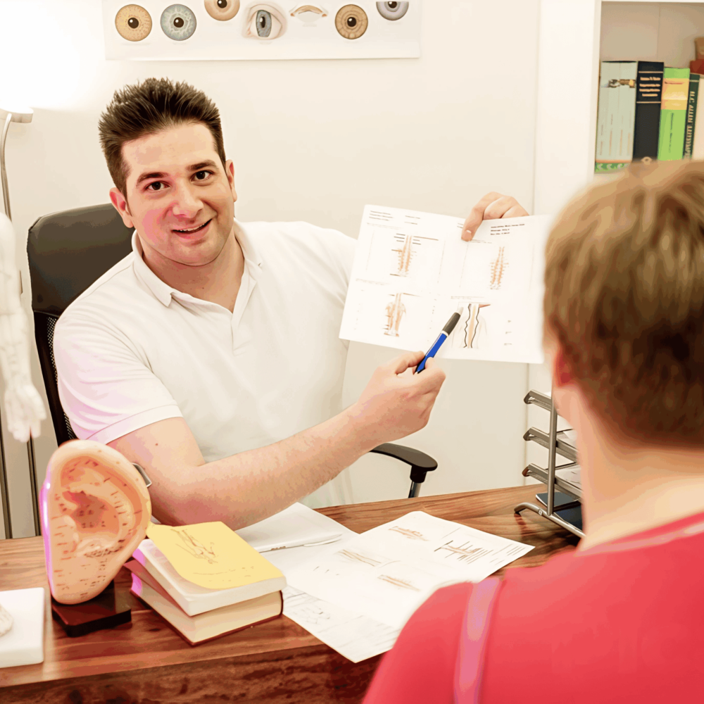 Chiropraktiker Metin Kenan Sisik erklärt einer Patientin in seiner Praxis in Ulm anhand von Grafiken und Modellen die Ursachen ihrer Beschwerden.